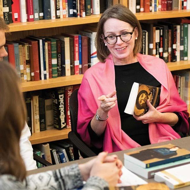 Three students sitting at a table with a professor discussing a religious book